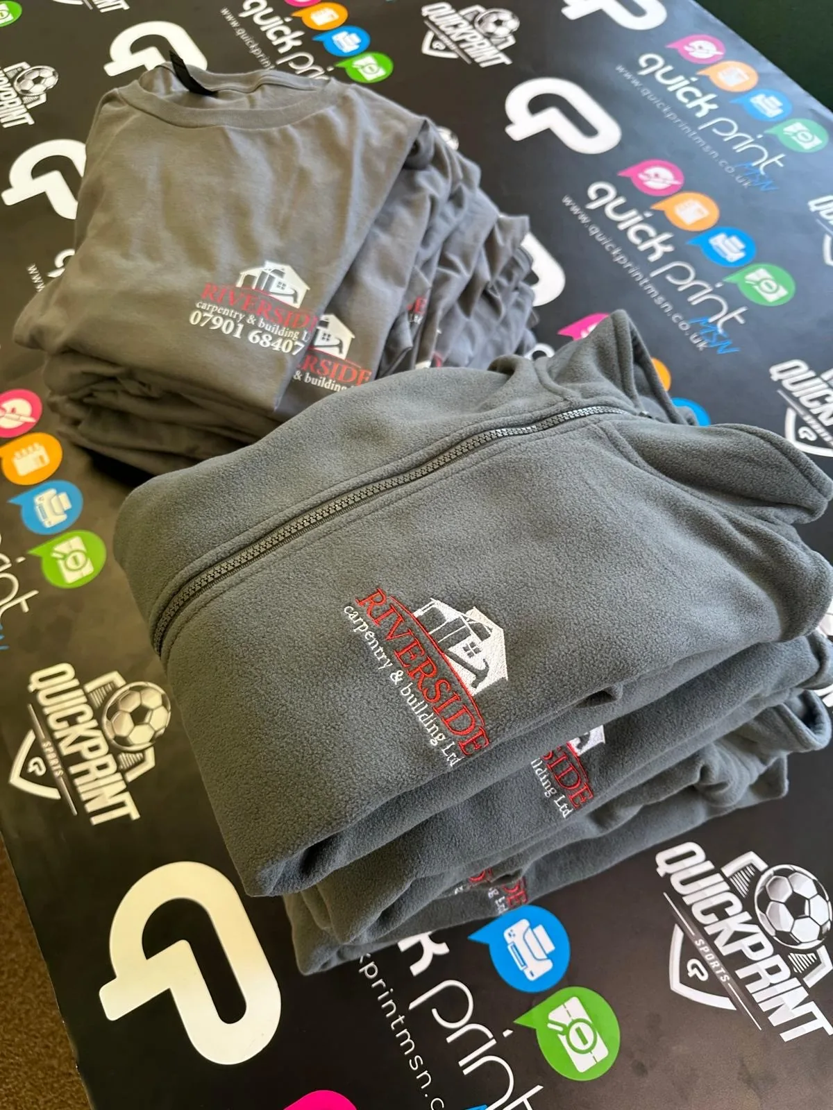 Stacks of grey Riverside Carpentry and Building branded workwear on a Quickprint display
